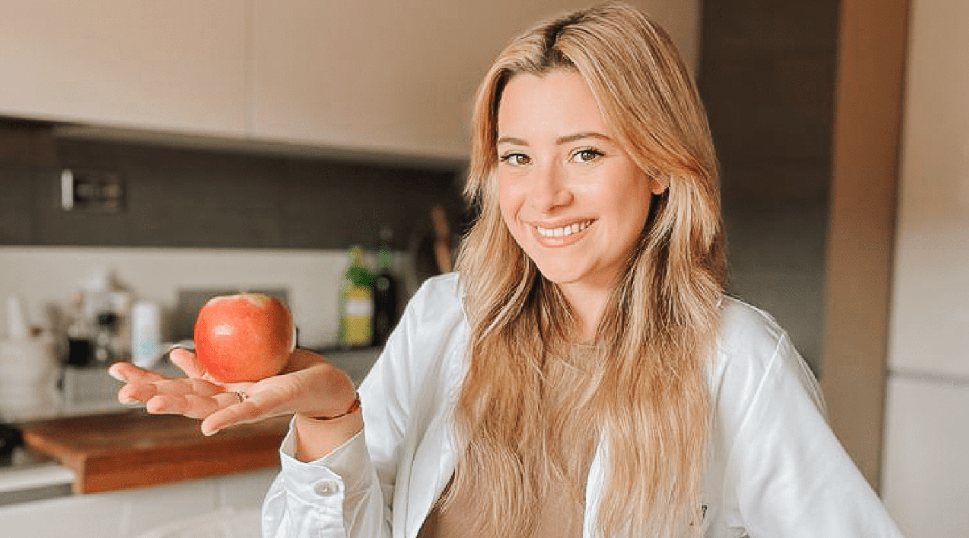 Una donna con in mano una mela nella sua cucina cerca consigli nutrizionali online da Chiara Petronio, nutrizionista di fiducia.